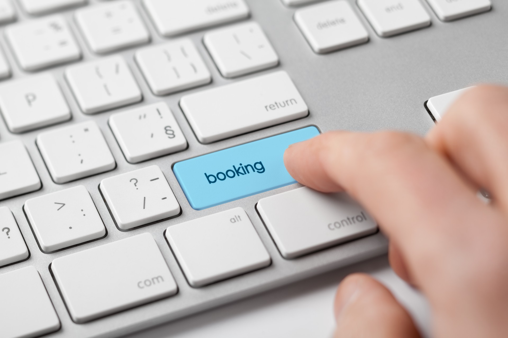 A close-up of a person pressing a blue "booking" button on a keyboard, symbolizing the process of making an online reservation or booking